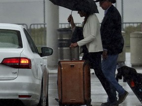 Travelers walk during a rainstorm to the terminals at Oakland International Airport, Friday, April 6, 2018, in Oakland, Calif. A fierce Northern California storm Friday shut down Yosemite National Park, threatened mudslides in wildfire-ravaged wine country and could present the first test of a partially repaired offshoot of the nation's tallest dam that nearly collapsed last year.