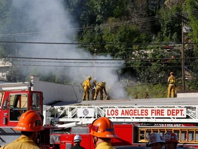 Los Angeles firefighters knock down hot spots on the roof of a music studio in Los Angeles Saturday, April. 14, 2018. Officials says two people were killed and at least three others were hurt when flames ripped through the studio. Fire spokeswoman Amy Bastman says crews found heavy smoke when they responded shortly before 7 a.m. Saturday in the Universal City area north of downtown.