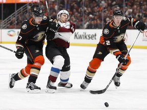 Anaheim Ducks' Josh Manson, right, chases the puck as Colorado Avalanche's Nathan MacKinnon, center, is shoved by Ducks' Hampus Lindholm, of Sweden, during the first period of an NHL hockey game Sunday, April 1, 2018, in Anaheim, Calif.