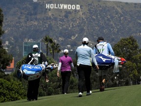 Stacy Lewis, second from left, and Shanshan Feng, second from right, of China, walk up the fairway on the ninth hole as the famed Hollywood sign sits in the background during the HUGEL-JTBC LA Open golf tournament at Wilshire Country Club, Thursday, April 19, 2018, in Los Angeles.