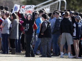 FILE - In this March 14, 2018, file photograph, a student waves a placard as classmates gather during a student walkout to protest gun violence on the soccer field behind Columbine High School in Littleton, Colo. Students at high schools across the country are expected to walk out of classes Friday, the 19th anniversary of the Columbine shooting, in their latest push for gun control. But they won't be protesting at the Colorado school where the violence took place.