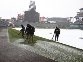 Grounds crew members use blowers to clear a light snow as it falls on Coors Field before the Colorado Rockies host the Atlanta Braves in the first inning of a baseball game Friday, April 6, 2018, in Denver.