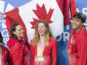 Canada's Penny Oleksiak, left, and Markus Thornmeyer, right, hold the flag above Taylor Ruck, who won eight medals, after the end of the swimming competition at the Commonwealth Games in Australia on April 10.
