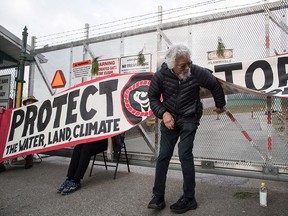 Environmentalist David Suzuki steps out from behind a banner after posing with protesters who blockaded an entrance to a Kinder Morgan facility in Burnaby, B.C., on March 19, 2018, to protest the Trans Mountain pipeline expansion.