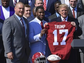 President Donald Trump, right, holds up a jersey he was presented with by Alabama team captains Bradley Bozeman, left, and Rashaan Evans, center, during an event for the 2017 NCAA National Champion University of Alabama football team on the South Lawn of the White House in Washington, Tuesday, April 10, 2018.