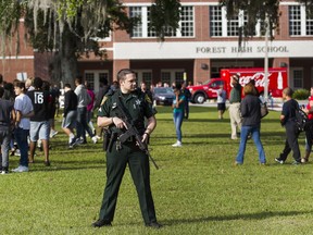 A Marion County Sheriff's Deputy stands outside Forest High School as students exit the school after a school shooting occurred, Friday, April 20, 2018 in Ocala, Fla.  One student shot another in the ankle at the high school and a suspect is in custody, authorities said Friday. The injured student was taken to a local hospital for treatment.