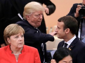 FILE - In this July 7, 2017 file photo German Chancellor Angela Merkel, front, looks on as U.S. President Donald Trump, center, pads the shoulder of France's President Emmanuel Macron prior to the first working session on the first day of the G-20 summit in Hamburg, northern Germany. Merkel is traveling to Washington to meet with Trump on Friday, April 27, 2018.
