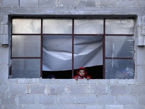 In this Friday, April 13, 2018 photo, a Syrian child who was displaced with his family from eastern Ghouta watches from the window of his family's shelter at a shelter in the village of Horjelli in the Damascus countryside, Syria. Thousands of Syrians displaced by the battle for the once-lush suburbs of Damascus now find themselves in a crowded settlement, where for the first time in recent memory they have enough to eat. The community is home to some 18,000 people displaced by the offensive that drove rebels out of eastern Ghouta. On Saturday, the Syrian government announced the capture of Douma, the last rebel stronghold in eastern Ghouta and the site of an alleged chemical attack that prompted a Western missile strike.