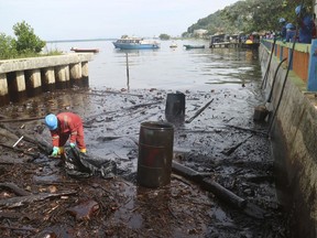 A worker cleans up oil that inundated the coastline in Balikpapan, Indonesia Wednesday, April 4, 2018. Waters off an Indonesian port city reek like a gas station after an oil spill and fire that killed four people over the weekend, an official said Wednesday. (AP Photo)