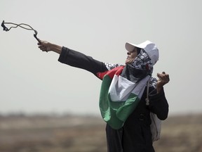 A Palestinian woman hurls stones at Israeli troops during a protest at the Gaza Strip's border with Israel, Friday, April 20, 2018. Since weekly mass marches began in late March, 28 Palestinians have been killed and hundreds wounded by Israeli army fire from across the border fence.