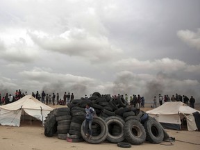 A Palestinian boy sits on a pile of tires to be burned during an ongoing protest next to Gaza's border with Israel, east of Khan Younis, Gaza Strip, Tuesday, April 3, 2018. Israel's defense minister said Tuesday that the military will not change its tough response to Hamas-led mass protests, warning that those who approach the border are putting their lives at risk. Eighteen Palestinians were killed by Israeli fire last Friday, the first day of what Hamas says will be six weeks of intermittent border protests against a stifling blockade of the territory.