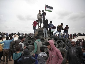 A protester holds a Palestinian flag on top of tires to be burned during an ongoing protest next to Gaza's border with Israel, east of Khan Younis, Gaza Strip, Tuesday, April 3, 2018. Israel's defense minister said Tuesday that the military will not change its tough response to Hamas-led mass protests, warning that those who approach the border are putting their lives at risk. Eighteen Palestinians were killed by Israeli fire last Friday, the first day of what Hamas says will be six weeks of intermittent border protests against a stifling blockade of the territory.