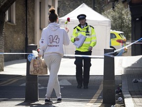 A woman carries a flower to a crime scene in Link Street, Hackney, east London, Thursday April 5, 2018. This week,  18-year-old Israel Ogunsola became London's 53rd murder victim of 2018. The British capital is being shaken by a spike in deadly violence, much of it involving young people caught up in gang feuds.