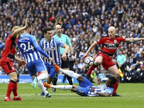 Huddersfield Town's Aaron Mooy shoots under pressure from Brighton & Hove Albion's Gaetan Bong, floor, during the English Premier League soccer match between Brighton and Hove Albion and Huddersfield Town at the AMEX Stadium, Brighton, England. Saturday, April 7, 2018.