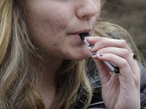 In this Wednesday, April 11, 2018 photo, an unidentified 15-year-old high school student uses a vaping device near the school's campus in Cambridge, Mass. Health and education officials across the country are raising alarms over wide underage use of e-cigarettes and other vaping products. The devices heat liquid into an inhalable vapor that's sold in sugary flavors like mango and mint -- and often with the addictive drug nicotine.