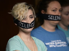 Amanda Thomashow, 28, left, and Alex Neil-Sevier, 29, wear silence gags while listening to the Michigan State University board meeting, Friday, April 13, 2018, Lansing, Mich. Interim Michigan State University President John Engler said Friday that he regrets the school's response to a woman filing a federal rape lawsuit against the university.
