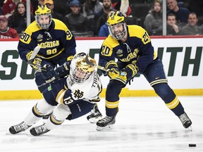 Michigan forward Cooper Marody (20) takes the skates out from under Notre Dame forward Colin Theisen (13), and is called for hooking during the first period of a semifinal in the NCAA men's Frozen Four hockey tournament Thursday, April 5, 2018, in St. Paul, Minn.