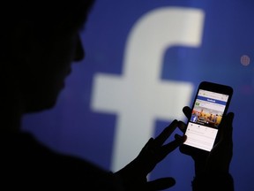 A user checks the Facebook Inc. site on their smartphone whilst standing against an illuminated wall bearing the Facebook Inc. logo in this arranged photograph in London, U.K., on Wednesday, Dec. 23, 2015.