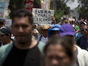 Central American migrants who participated in the annual Migrants Stations of the Cross caravan, one with a sign that says in Spanish: "Get out Donald Trump," walk to the Basilica of Guadalupe after arriving to a shelter in Mexico City, Monday, April 9, 2018. Mexico's capital is the final planned stop of the migrant caravan that left from the Mexico-Guatemala border late last month to draw attention to policies toward immigrants and refugees.