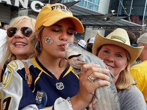 FILE - In this June 5, 2017, file photo, Nashville Predators fan Anna Claire Massey kisses a catfish as fans celebrate before Game 4 of the NHL hockey Stanley Cup Finals between the Nashville Predators and the Pittsburgh Penguins, in Nashville, Tenn. Tossing catfish has long been a popular hockey tradition in Music City, and the Predators finally have their own catfish tank inside the arena.  President Sean Henry unveiled the new tank hours before the Predators open the NHL postseason against Colorado in their first-round Western Conference series. The team put the first of four catfish into the tank Wednesday with the second coming before Game 1 on Thursday night, April 12, 2018.