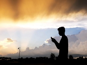 FILE- In this July 17, 2015, file photo, a teenager checks his cell phone as storm clouds pass in Zionsville, Ind. A new poll by the Associated Press-NORC Center for Public Affairs Research says 12 percent of Americans use Facebook "almost constantly," while 34 percent use it several times a day. About 15 percent use it once a day, and only 9 percent of Americans don't use Facebook.