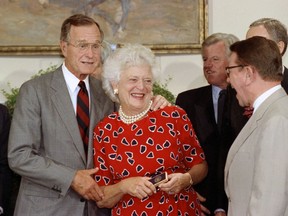 FILE - In this July 26, 1991 file photo, first lady Barbara Bush, center, laughs with Sen. Paul Simon, D-Ill, right, after receiving the pen President George Bush, left, used to sign the National Literacy Act of 1991 during a ceremony at the White House in Washington. Promoting literacy was a longtime cause for Barbara Bush, who died Tuesday, April 17, 2018, at age 92. She met many authors during her time in Washington and in the years following. Sandra Brown, Mary Higgins Clark and Harlan Coben were among those who became good friends, and shared memories of a former first lady whom Brown said "put her heart and soul" into getting people to read while also being "very funny, very candid with her comments."