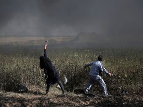 FILE - In this Friday, April 6, 2018 file photo, a Palestinian woman and a man hurl stones towards Israeli troops during a protest at the Gaza Strip's border with Israel. The flareup of deadly violence in Gaza is of a new kind, even in the inventive annals of Mideast conflicts: Israeli soldiers shooting at Palestinian demonstrators burning tires and hurling firebombs across what looks like an international border, inflicting casualties while claiming concerns of a mass breach of the barrier.