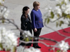 German Chancellor Angela Merkel, right, the Prime Minister of New Zealand, Jacinda Ardern, left, are pictured behind blossoms as they attend a military welcome ceremony in Berlin, Germany, Tuesday, April 17, 2018.