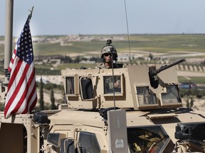 A U.S. soldier sits in an armoured vehicle on a road leading to the tense front line with Turkish-backed fighters in Manbij, north Syria, Wednesday, April 4, 2018.