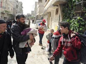 FILE - This Saturday, March. 24, 2018 file photo, released by the Syrian official news agency SANA, shows civilians carrying their belongings as they left the rebel-held suburb of Douma, east of the capital Damascus, Syria. Syrian state media said Monday, April 2, 2018, that the largest rebel group in Damascus' eastern Ghouta, the Army of Islam, has begun to evacuate from Douma. The government is waiting for the rebels to leave the besieged town before it can say it has full control of the area, after seven years of revolt. (SANA via AP, File)
