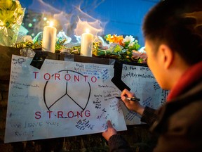 A man writes a message on a sign during a vigil on April 24, 2018, near the site of the previous day's deadly van attack on Toronto's Yonge Street.