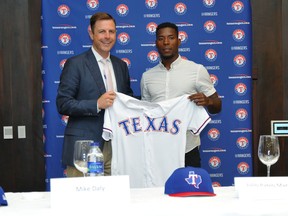 In this photo provided by the Texas Rangers, Mike Daly, Texas Rangers assistant general manager, presents Julio Pablo Martinez with a team jersey after a news conference in Santo Domingo, Dominican Republic, Thursday, April 19, 2018. Martinez agreed to a minor league contract with the Rangers that includes a $2.8 million signing bonus and will make his debut for the organization in the Dominican Summer League. (Texas Rangers via AP)
