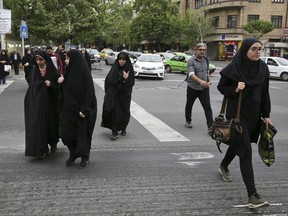 In this Sunday, April 22, 2018, photo, pedestrians cross a street in Tehran, Iran. A grainy video of female officers from Iran's morality police assaulting a young woman whose headscarf only loosely covered her hair has sparked a new public debate on the decades-long requirement for women in the Islamic Republic.