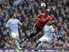 Manchester United's Paul Pogba heads the ball between Manchester City's Bernardo Silva, left, and Manchester City's Ilkay Gundogan during the English Premier League soccer match between Manchester City and Manchester United at the Etihad Stadium in Manchester, England, Saturday April 7, 2018.