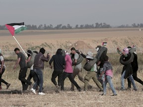 Palestinian masked protesters carrying tires walk toward the border fence during clashes with Israeli troops along Gaza's border with Israel, east of Khan Younis, Gaza Strip, Thursday, April 5, 2018. An Israeli airstrike in northern Gaza early on Thursday killed a Palestinian, while a second man died from wounds sustained in last week's mass protest. The fatalities bring to 21 the number of people killed in confrontations in the volatile area over the past week with a new round of protests along the border is expected on Friday.