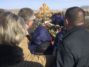 The family of 10-year-old Vadim Chmykhalov stand in front of his grave at a cemetery on the outskirts of the Siberian city of Kemerovo, about 3,000 kilometers (1,900 miles) east of Moscow, where a fresh row of graves have the marks of March 25, the date of the fire, in Russia, Thursday, March 29, 2018. The Siberian city of Kemerovo was on Thursday burying some of the victims of Sunday's shopping mall fire that killed 64 people, many of them children.