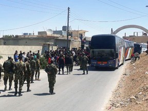 This photo released by the Syrian official news agency SANA, shows Syrian government forces overseeing the evacuation by bus of rebels and their family from the towns of Ruhaiba in the eastern Qalamoun region in the Damascus countryside, Syria, Saturday, April 21, 2018. Syrian state media says several buses have left the towns of Ruhaiba, Jayroud, and al-Nasriya carrying hundreds of rebels and their families to opposition territory in north Syria. (SANA via AP)