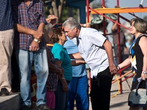 FILE - In this March 11, 2018 file photo, Cuba's Vice President Miguel Diaz-Canel, center, holding hands with his wife Lis Cuesta Peraza, speaks with a woman as he waits in line with voters at a polling station during elections for national and provincial representatives for the National Assembly in Santa Clara, Cuba. Raul Castro has pledged to step down on April 19, 2018, and hand the presidency to Diaz-Canel, who will confront a stagnant economy, decaying infrastructure, a hostile U.S. administration and widespread disenchantment with a centrally planned system that can't provide state employees with a living wage, but forbids most forms of private enterprise.