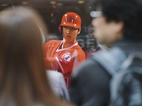 In this April 4, 2018 photo, pedestrians in Tokyo watch a TV showing the live broadcasting of Los Angeles Angels' Shohei Ohtani, of Japan, gets ready to bat during a baseball game against the Cleveland Indians. Shohei Ohtani's games are shown live in the morning by national broadcaster NHK. In the afternoon, talk shows dissect his every move while evening sports programs feature highlights of his latest accomplishments.