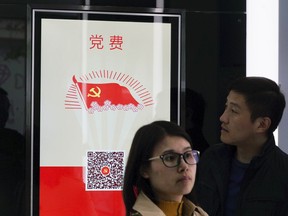 In this April 13, 2018, photo, a bank customer looks at a touchscreen which allows users to pay Communist Party membership fees at an automated branch in Shanghai.  The outlet opened by Beijing-based China Construction Bank has been dubbed China's first "unmanned bank" and is equipped with face-scanning software, a virtual reality room and talking robots.