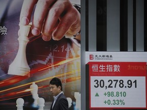 A man walks past an electronic board showing Hong Kong share index outside a local bank in Hong Kong, Wednesday, April 4, 2018. Asian stock markets were mixed in early trading Wednesday as investors digested the latest volley of tariff measures and threats between the U.S. and China.
