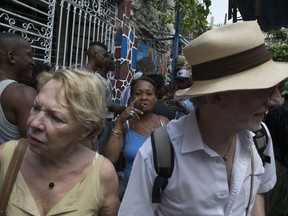 FILE - In this March 22, 2015 file photo, tourists visit Hamel Alley as a Cuban woman smokes a cigar in the background, in Havana, Cuba. Tourism numbers have more than doubled since Castro and President Barack Obama re-established diplomatic relations in 2015, making Cuba a destination for nearly 5 million visitors a year, despite a plunge in relations under the Trump administration.