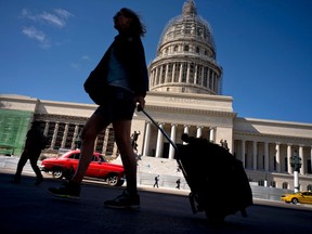 FILE - In this Jan. 18, 2018 file photo, a tourist walks with her suitcase in front of the Capitolio in Havana, Cuba. President Donald Trump drew cheers from a Cuban-American crowd last summer when he announced that he was rolling back some of Barack Obama's opening to Cuba in order to starve the island's military-run economy of U.S. tourism dollars and ratchet up pressure for regime change.