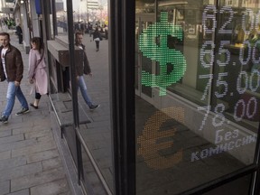 People walk past an exchange office screen showing the currency exchange rates, in Moscow, Russia, Tuesday, April 10, 2018. The ruble has plunged for the second day in a row following fresh U.S. sanctions against Russia.