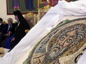 Cyprus' Archbishop Chrysostomos II is seen in the background next to the extremely rare 6th century mosaic depicting St. Andrew, during a ceremony of repatriation at the Archbishop in capital Nicosia, Cyprus, Monday, April 23, 2018. Archbishop Chrysostomos II told a ceremony Monday that the artistry coupled with the rarity of the mosaic - one of only a handful which survived a period in the 8th and 9th century which saw the destruction of many such mosaics and icons - had become a symbol of Cyprus' "stolen heritage."