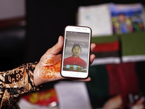 In this March 31, 2018 photo, Adila Hamidi shows a photo of her son, 17-year-old Faisal who was killed in a suicide attack, while standing in front of mementos for his "memory box," part of an initiative designed by the Afghanistan Human Rights and Democracy Organization, in Kabul, Afghanistan. Survivors of Afghanistan's many wars have tucked memories of those they have lost inside boxes draped in a flag of their own creation that represents the Afghanistan of their dreams. The boxes are a tribute to those lost to war but also a healing balm for those left behind.