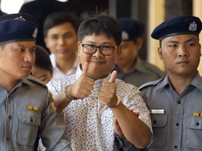Reuters journalist Wa Lone, center, thumbs up as he is escorted by police upon arrival at the court for trial in Yangon, Myanmar Friday, April 20, 2018. Myanmar court continues hearing on case against two Reuters journalists, arrested under the colonial-era Official Secrets Act, for having restricted documents in their possession.
