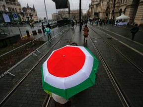 FILE- In this Thursday, March 15, 2018, file picture a supporter of Hungarian Prime Minister Viktor Orban walks under an umbrella in Hungary's national flag colors outside the Hungarian Parliament building in Budapest, Hungary, during celebrations of the Hungarian national holiday, the 170th anniversary of the outbreak of the 1848 revolution and war of independence against the Habsburgs. Hungarian Prime Minister Viktor Orban is betting that his relentless campaign against immigration will keep his supporters united and motivated for Sunday's national election. Polls show Orban's Fidesz party with a sizable lead over Jobbik, a nationalist right-wing party, as well as the Socialist Party and other, smaller left-wing or green groups. Orban is seeking his third consecutive term and his fourth overall since 1998.