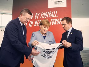 FILE - In this March 26, 2018 file photo German chancellor  Angela Merkel, center, German Football Federation head, Reinhard Grindel, left, and former soccer player Philipp Lahm, right, promote the European Soccer Championship 2024 in Berlin. Germany wants to host the 2024 European Championship and bring people closer together amid populist waves across the continent. Believing sports can be a positive force in political debate, German soccer federation president Reinhard Grindel told The Associated Press on Monday April 23, 2018  "this is what a Euro can deliver."