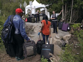 In this Aug. 7, 2017 file photo, a Royal Canadian Mounted Police officer informs a migrant couple of the location of a legal border station, shortly before they illegally crossed from Champlain, N.Y., to Saint-Bernard-de-Lacolle, Quebec, using Roxham Road. Authorities say more than 80 percent of the 4,000 migrants who crossed into Quebec recently are from Haiti, and the rest include people from India, Mexico, Colombia and Turkey.
